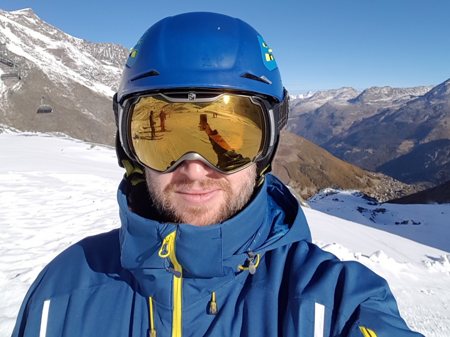 a man out on the ski slopes with a blue coat and hood up with golden skiing goggles