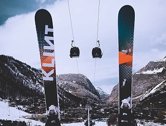 A pair of skis raised in the air, in the background is a ski lift, mountains and clear blue sky